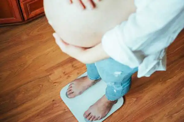 Image of woman weighing herself and experiencing weight gain through pregnancy Healey